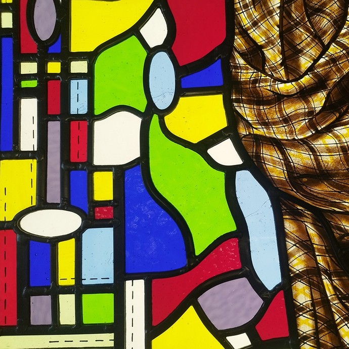 Pieces of stained glass in primary colours divided by black cames; half the glass is covered by a thin piece of chequered cloth. 