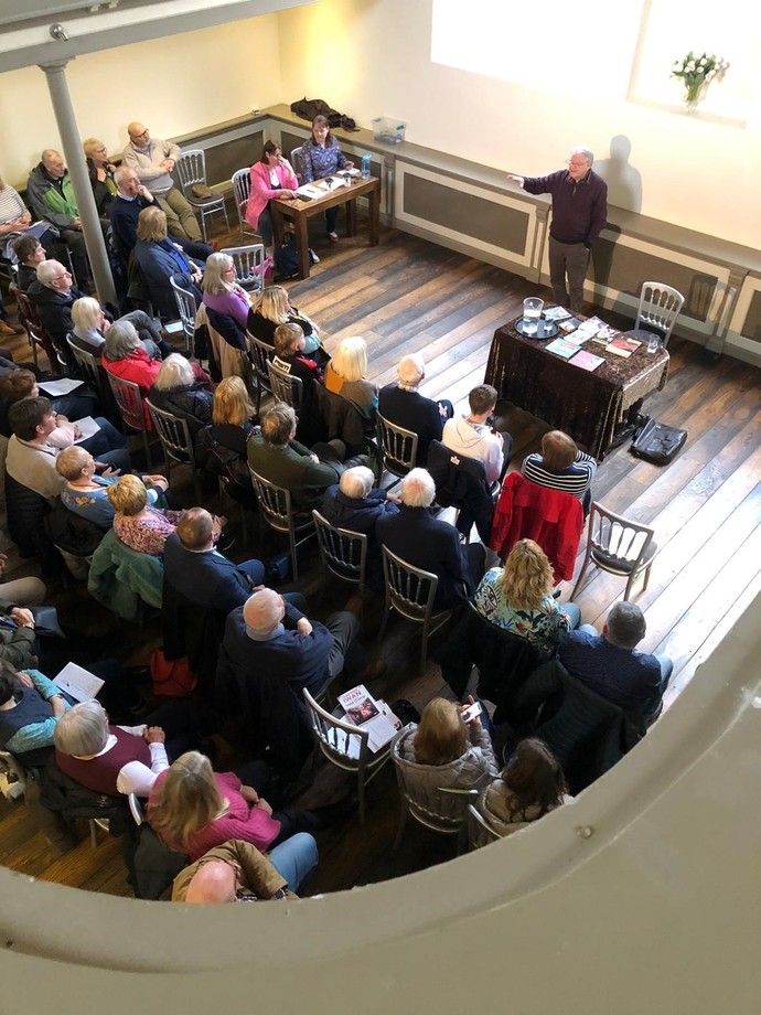 A crowd shot looking at Dafydd Iwan speaking in the event with the simultaneous translators at work
