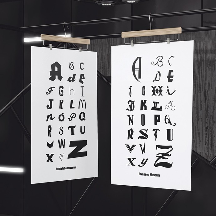 Two font designs are suspended from wooden hangers in a dark studio. 