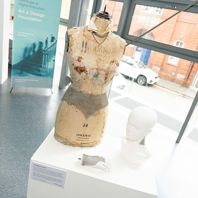 Model yn cael ei arddangos ochr yn ochr â phen a llaw model; mae ei wyneb wedi'i orchuddio â papur melynaidd, fflawiog; mae darn bach o faelwisg i'w weld ar y tri gwrthrych; yn ogystal, mae'r model yn gwisgo mwclis o gysylltiadau metel. 