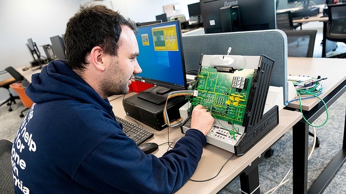 Mae dyn yn plygio cebl i mewn i Digiac, uned hyfforddi electroneg.