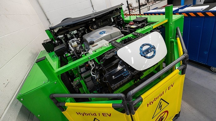 Injan fawr gyda brandio Nissan; mae arwydd melyn o’i flaen yn dweud: Hybrid/EV ac yn dangos symbol rhybudd mellten. 
