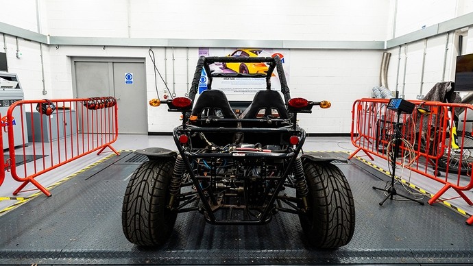 Math o gerbyd go-cart mawr gyda theiars mawr; mae ganddo ddwy sedd ac injan yn y cefn sy’n agored i'w gweld o dan y ffrâm fetel. 