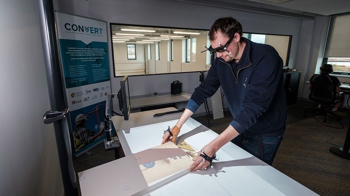 A man in VR glasses and wearing sensors on his hands uses a wood machine simulator to practise cutting a timber plank.