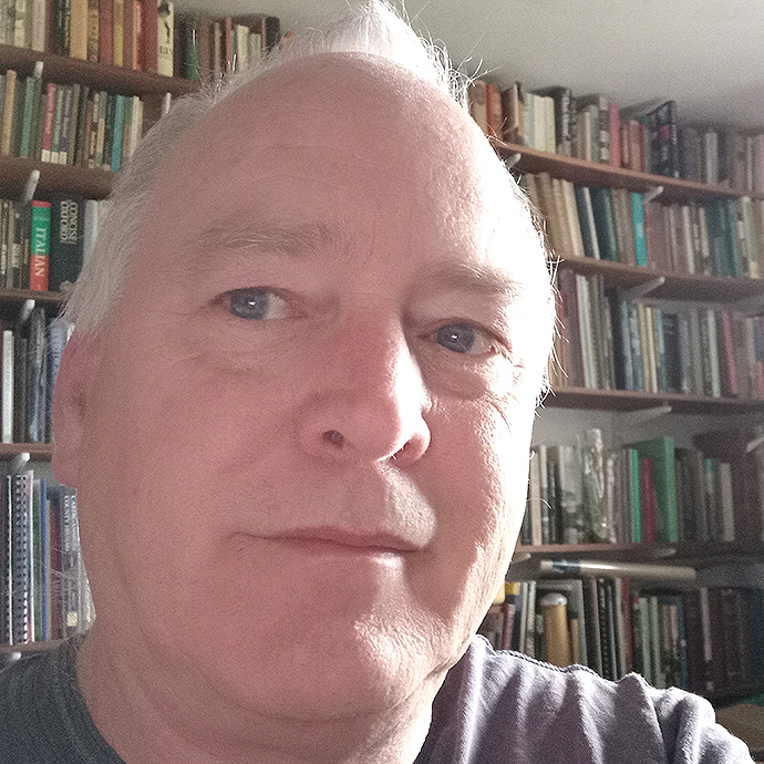 Martin Lockock mewn ystafell gyda llyfrau mewn silffoedd ar y waliau.