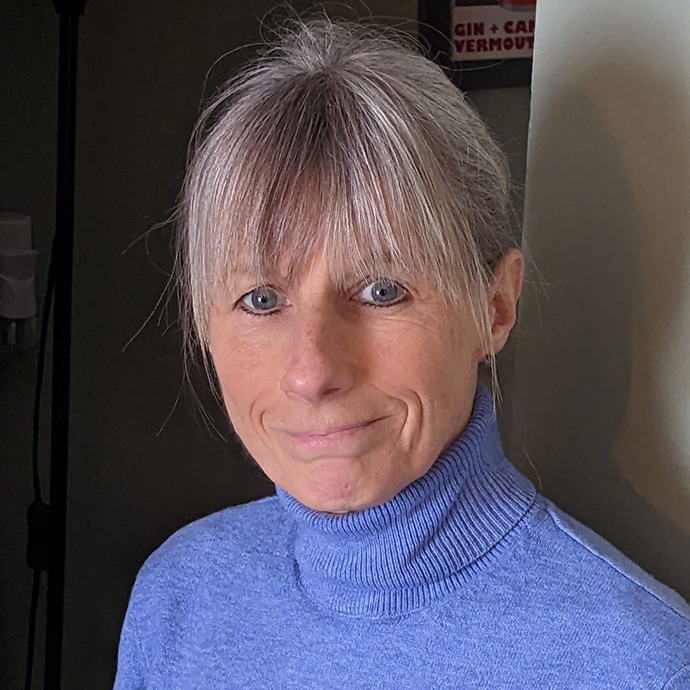 Wearing a cornflower blue polo neck, Sue Ainsworth looks towards the camera.