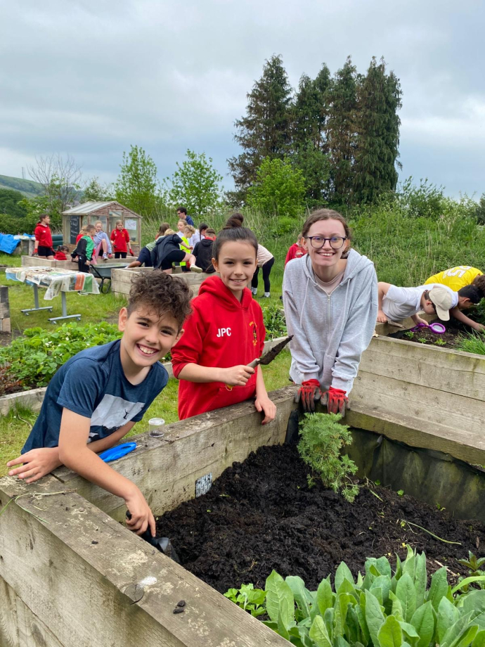 a student and two pupils taking part in a gardening workshop in Yr Egin's garden