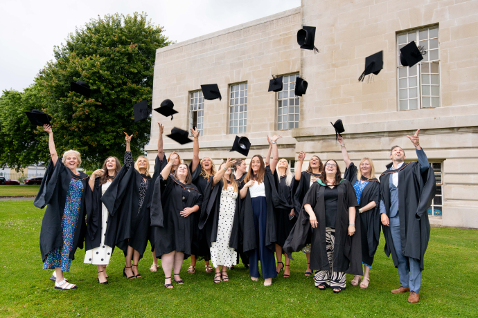 a group of the students outside the Brangwyn Hall throwing caps