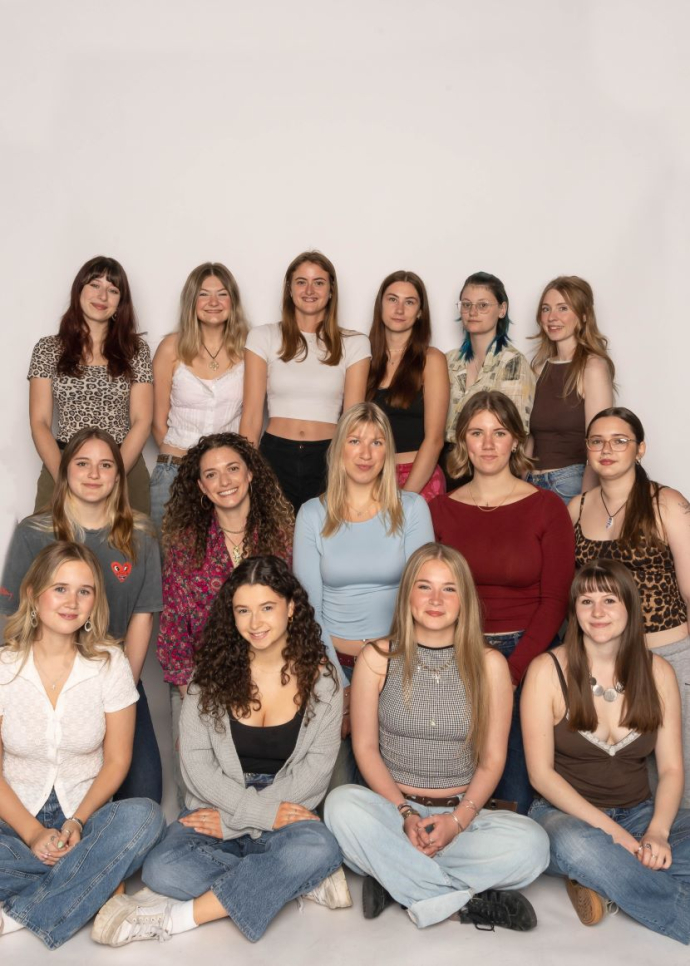 A group of happy, smiling students sat and standing against a white background.