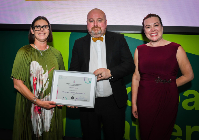Two women and a man standing proudly at an awards ceremony, holding the award certificate, against a green background.
