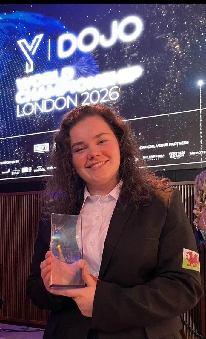 A smiling student holding an award with an electronic screen in the background.