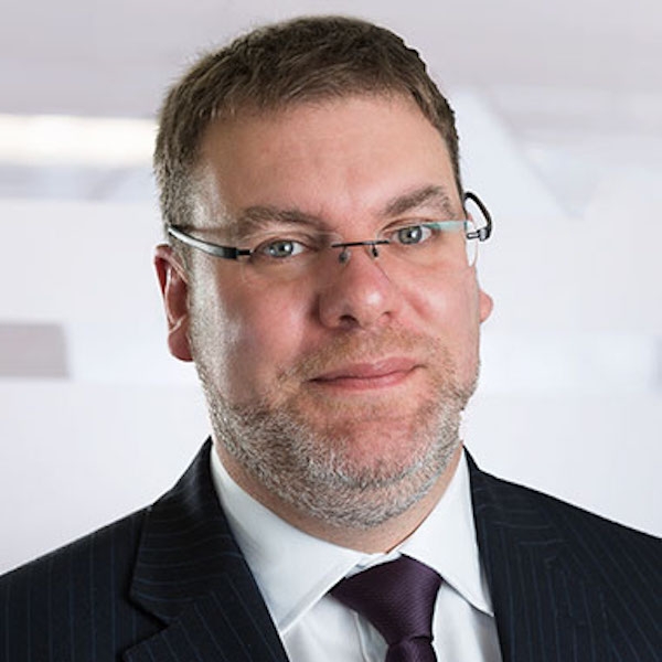 A cropped portrait image of a man wearing glasses and a suit and tie.