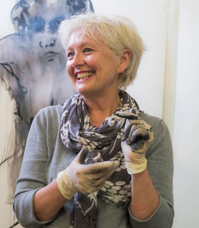 A smiling lady wearing craft gloves wearing a scarf.