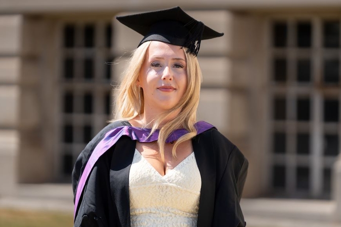A smiling and proud graduate standing in her cap and gown.