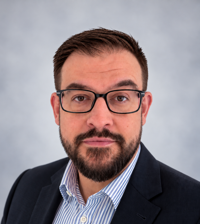 A headshot of a man wearing glasses, wearing a suit coat and shirt.