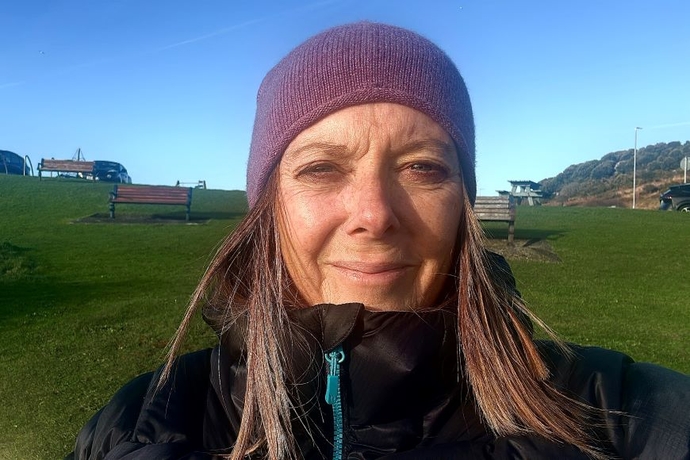 A lady with long hair, wearing a hat, standing outside, with green grass behind and blue sky above.
