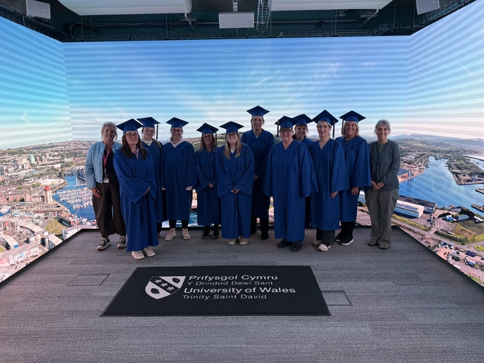 cohort in their cap and gown in immersive room 