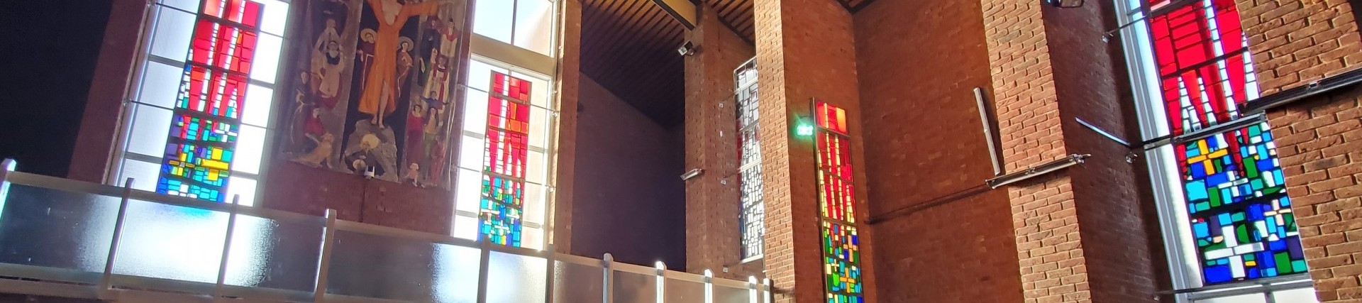 Brick interior of a church with colourful stain glass panels suspended in front of plain windows.