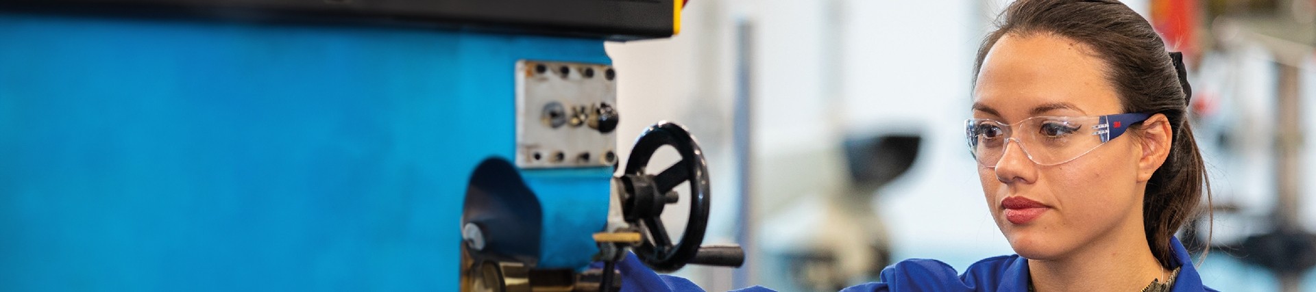 Apprentice working machinery wearing blue overalls