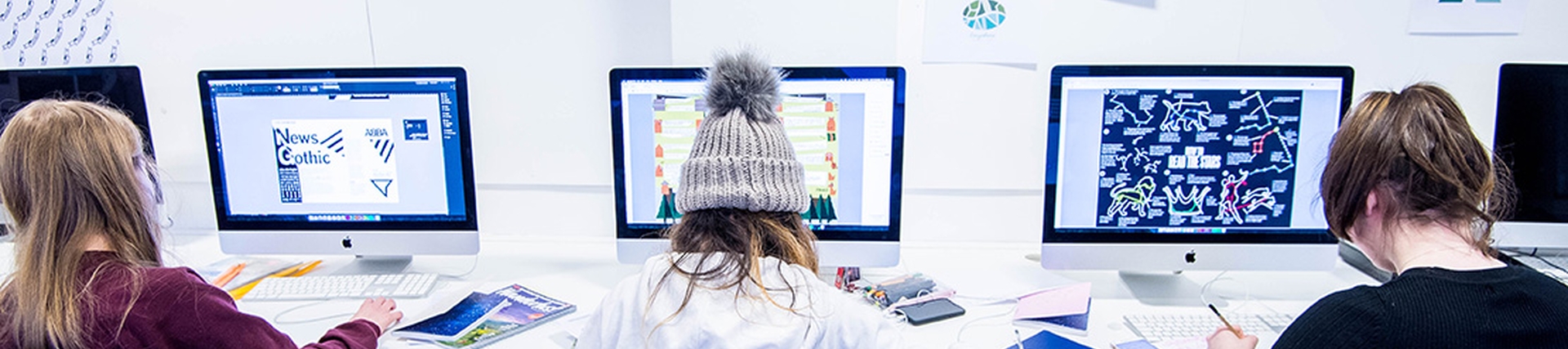 Three students creating designs on Apple Mac computers.