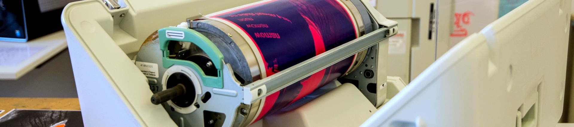 A colourful poster wrapped around a metal cylinder in a modern printing press. 