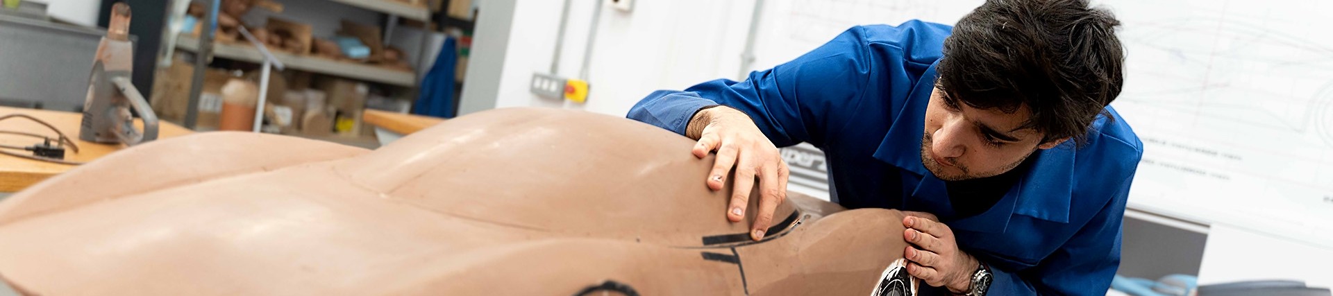 A young man works refining a large model of a sportscar. 