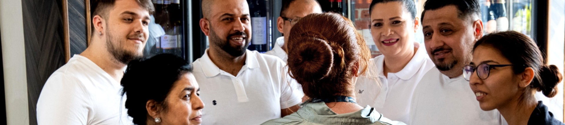 Hospitality staff smile as they listen to a restaurant manager. 