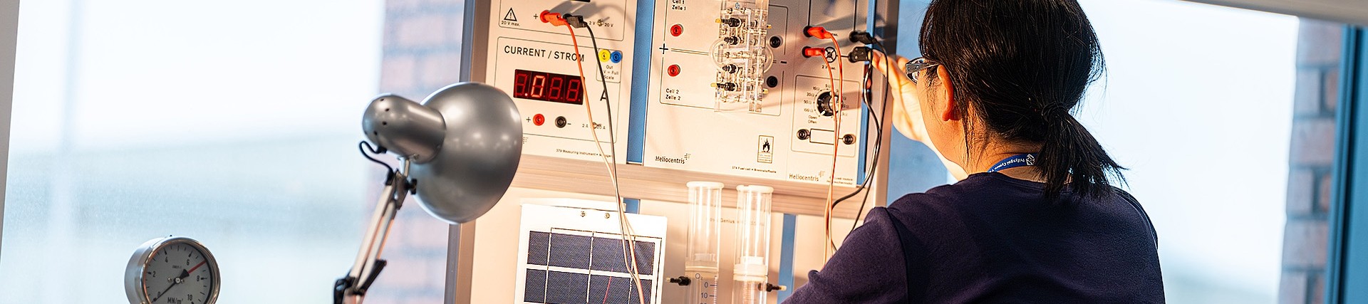A woman plugs a cable into a white scientific data board which includes fields related to voltage, current and air; the product is called Hydro-genius Professional.