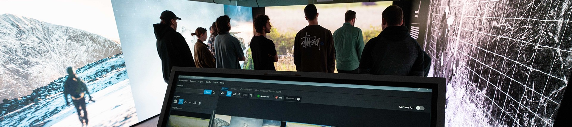 A group of students stand in an Immersive Room looking at the digital walls which display dramatic images of the outdoors.