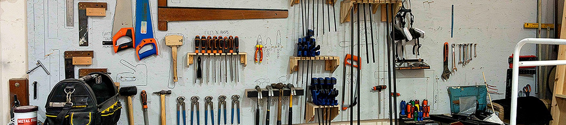 Tools including saws, spanners, and screwdrivers hang from a board in neat groups according to category; above them, a sign reads: in case of zombie apocalypse, we're gonna need a bigger board.