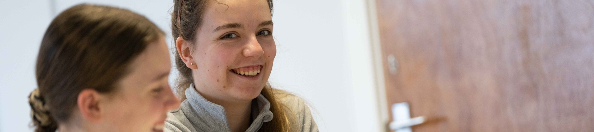 image of woman, sitting next to another student, smiling in a Carmarthen Teaching classroom