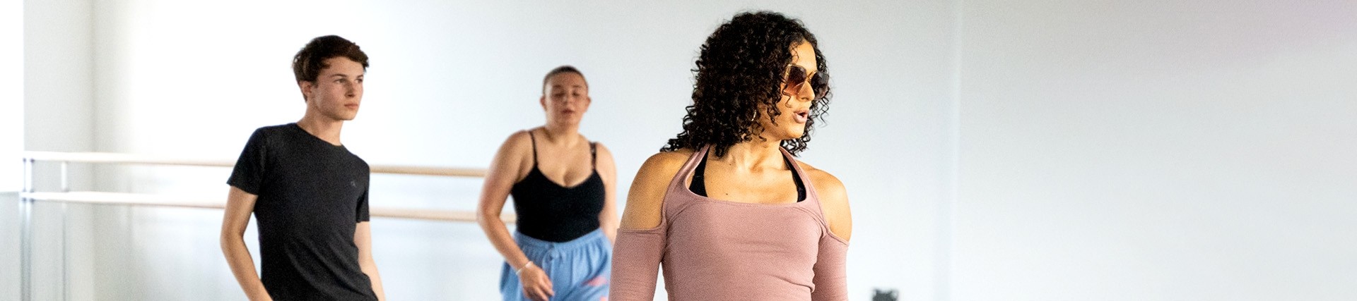 Three students practise dance moves: a swaggering step to the right with finger snaps.