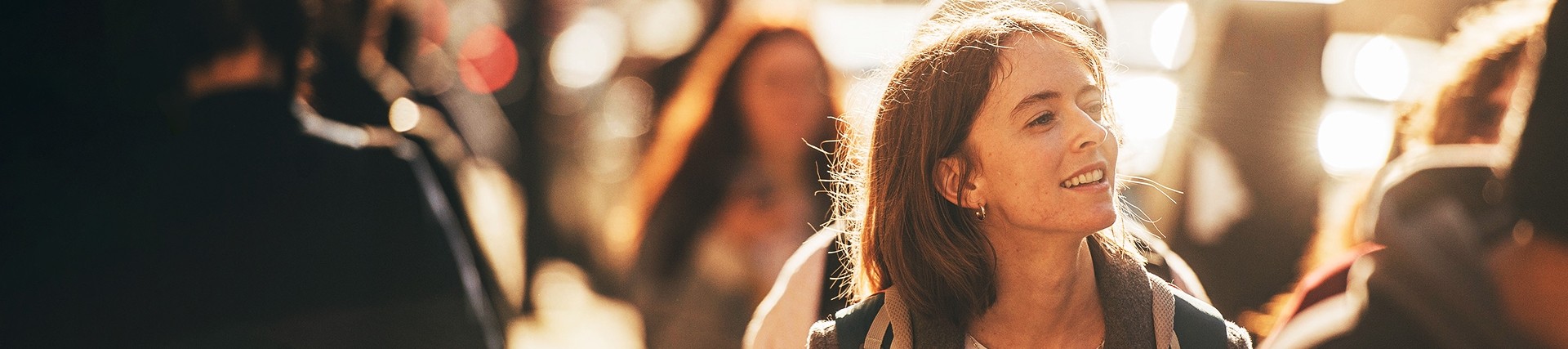A young woman smiles in the middle of a busy pedestrian street.