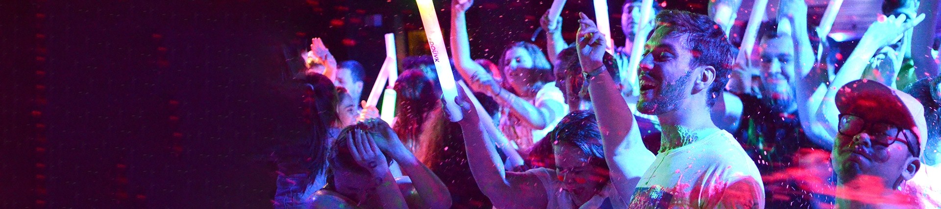 Young people waving light sticks dance in a night club.