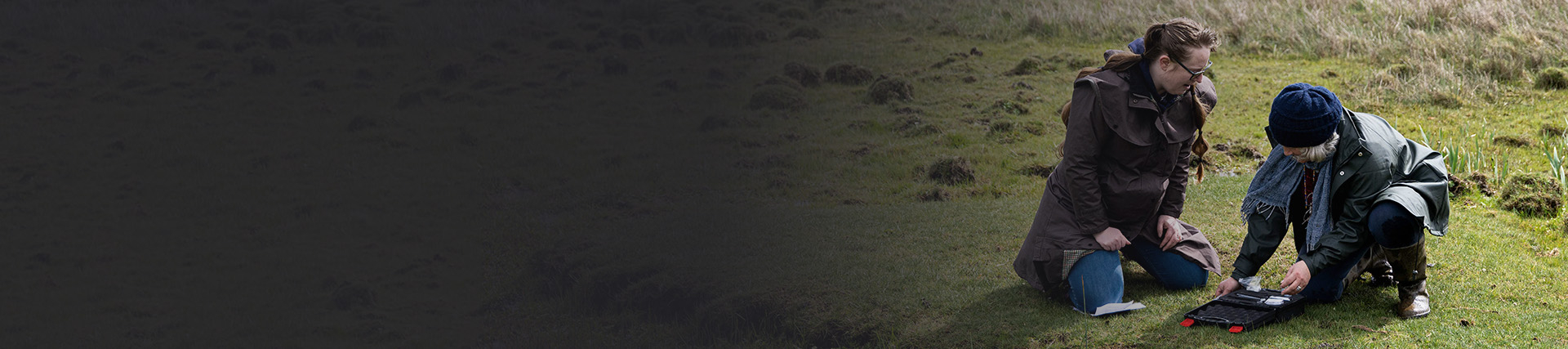Two women crouch over a sampling kit on an area of heathland.