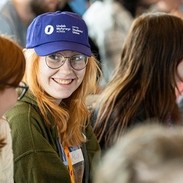 Myfyriwr mewn cap Undeb y Myfyrwyr yn gwenu