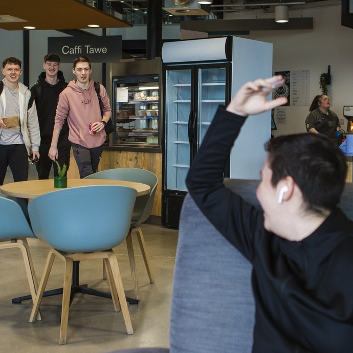 student waving at friends inside swansea campus cafe 