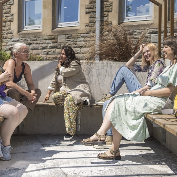 five students sitting on bench outside in the sun