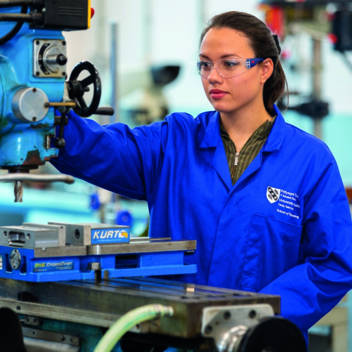 Apprentice working machinery wearing blue overalls