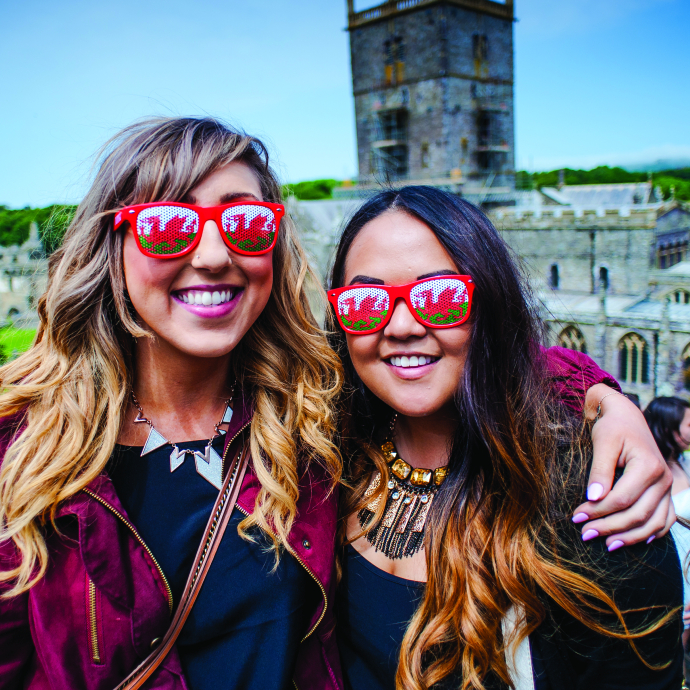Students smiling in front of a castle wearing Welsh dragon sunglasses