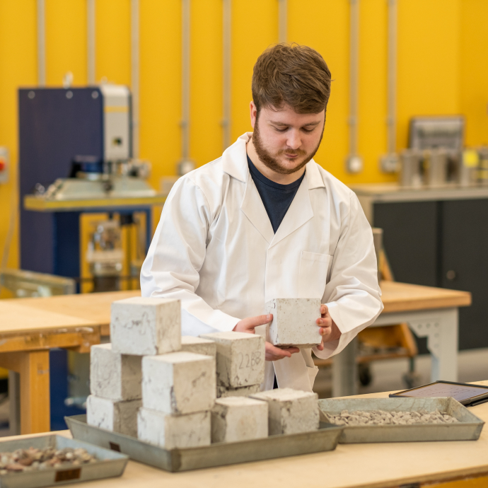 Student in lab coat holding a cube structure 