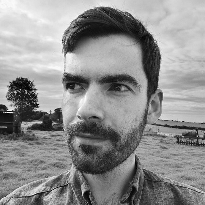 A black-and-white photo of Dr Gareth Evans-Jones with fields stretching out behind him. 