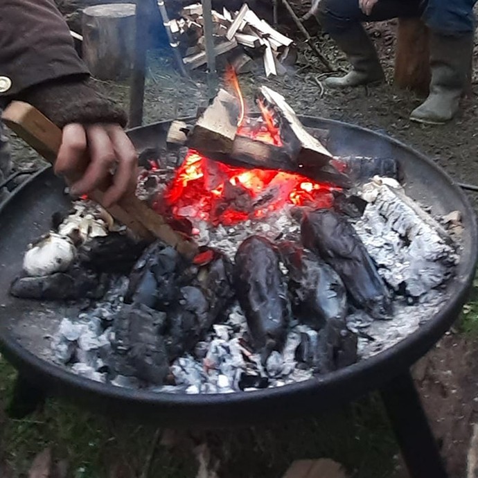 A man and two women build a fire in a metal bowl using twigs.