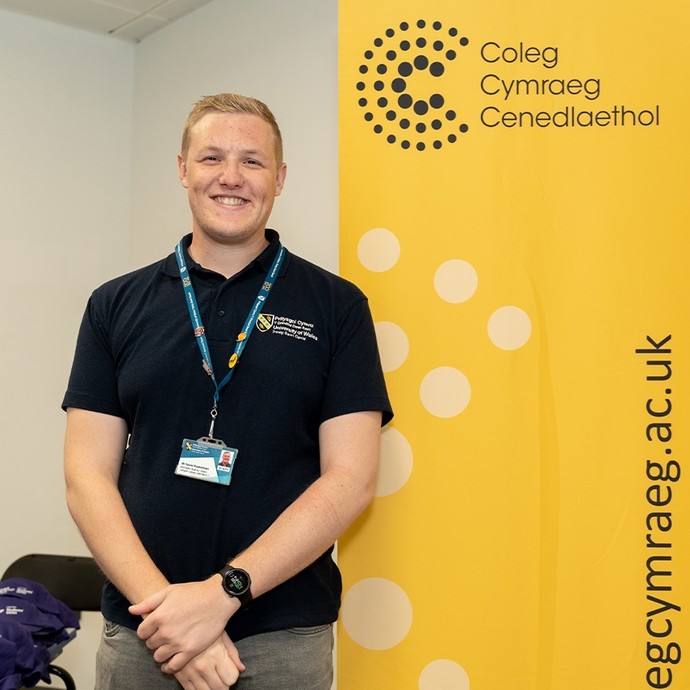 Staff member standing next to a Cymraeg banner