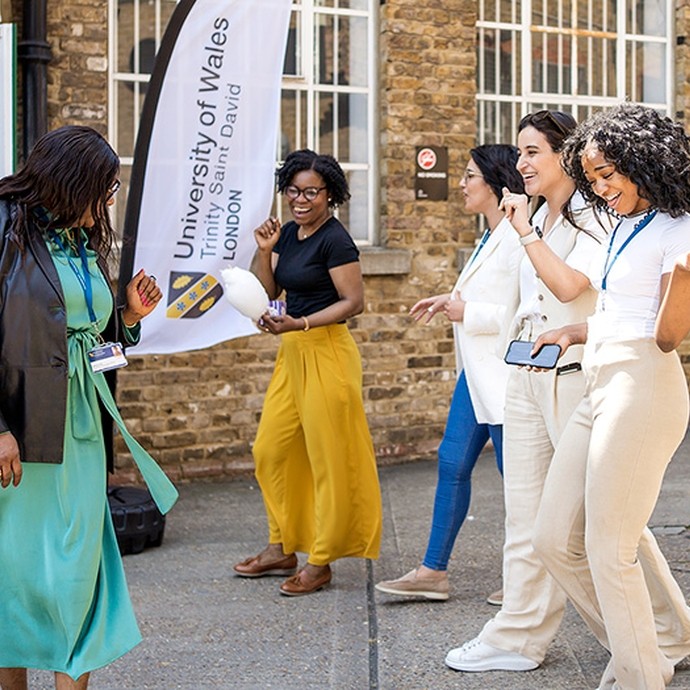 Four women laugh as they cross paths outside the door of a university building.