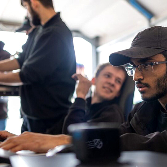 Wearing a baseball hat and glasses, Ragulan types on a keyboard, looking towards a screen with a look of concentration.