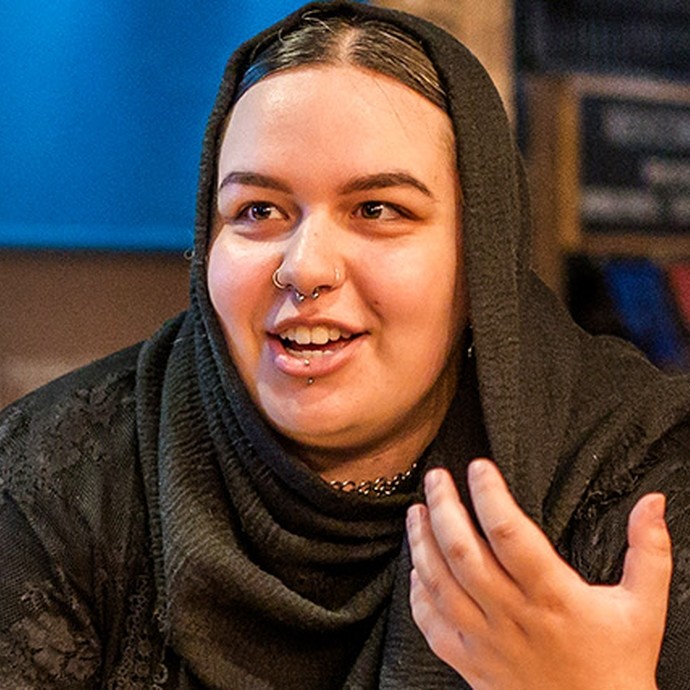 A young woman wearing a hijab chats to a friend in a modern café-bar.