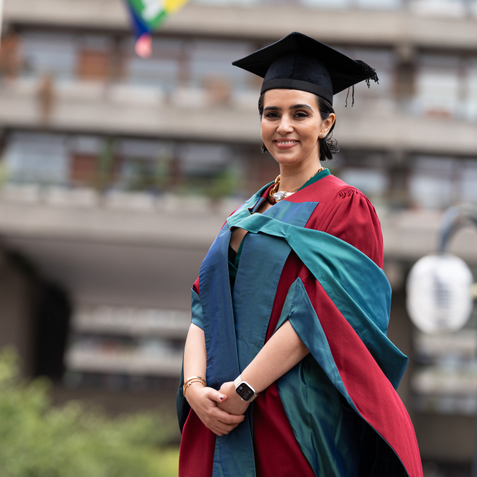 A happy, smiling graduate standing proudly, dressed in her cap and gown at graduation..