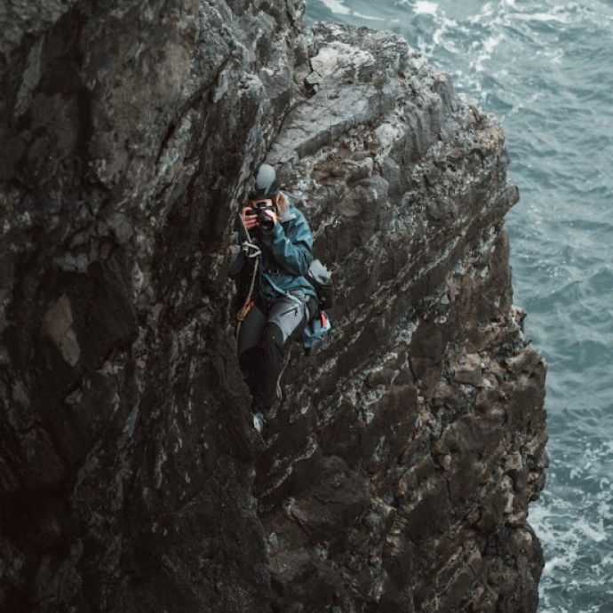 A person climbing a cliff overhanging the sea
