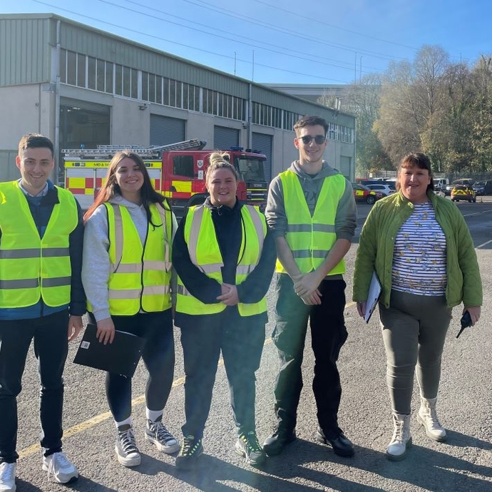 A group of people wearing high vis jackets standing in front of a fire engine at a training centre